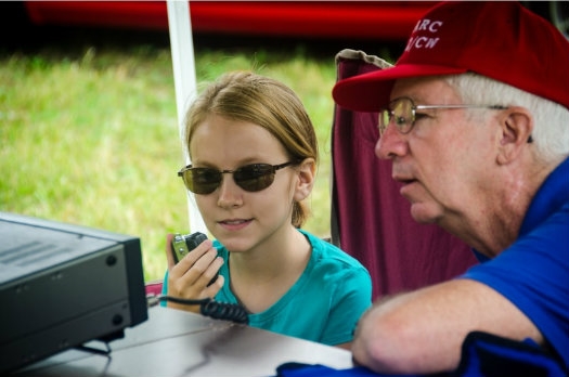 A man is sitting next to a young girl who is speaking on a microphone.