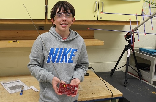 A boy wearing gogles and holding up a circuit board.