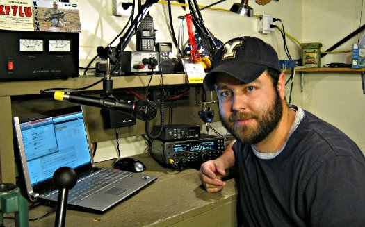 A man is facing the camera and smiling next to a radio station set up inside.