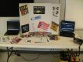 Public information table set-up by KG4EDY including ARES literature, laptops running ARRL PSA videos and satellite tracking software, and 2m rig for communicating with local repeater.