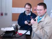 Two people standing next to a radio setup inside.